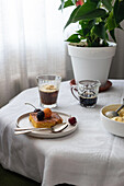 On the coffee table is a delicious slice of cake with fresh berries, accompanied by a glass of coffee and a bowl of ice cream, creating a light and pleasant atmosphere.