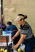 A woman skilfully prepares fresh coconut water from whole coconuts and bottles it to offer a refreshing drink. This scene captures a moment of local tradition and natural refreshment.