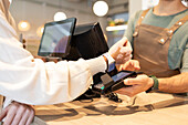 A café employee helps a customer make a contactless payment with a smartwatch The scene emphasises the modern convenience and customer service in a cosy café