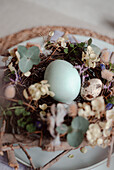 Close-up of a detailed Easter nest with naturally coloured eggs amidst a variety of flowers and plants, elegantly arranged on a calm table top.