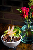 A beautifully presented bowl of Asian beef, garnished with fresh greens and pear slices, paired with a vibrant bouquet of flowers in a glass vase on a wooden table