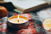 A burning candle on a cosy, colourful, checked fabric during the Christmas season, capturing the essence of Christmas warmth and festive spirit, shot from above.