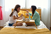 A lesbian couple happily having breakfast in bed, emphasising closeness and warmth in a sunlit room - a perfect representation of LGBTQIA+ love and everyday life