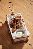 Delicious, crispy, golden-brown chicken wings, served in a basket with a creamy dipping sauce, garnished with fresh herbs, a perfect savoury snack to share