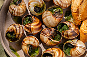 Baked snails in close-up with butter and fresh parsley, served with crusty bread.
