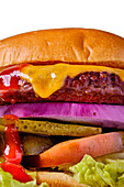 Close-up of a juicy cheeseburger with melted cheddar cheese, red onions, pickles, tomatoes, lettuce and ketchup, served on a toasted golden bun
