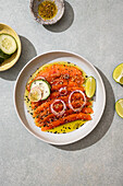 A vibrant dish of thinly sliced salmon carpaccio, garnished with lime, cucumber and onions, drizzled with oil and seeds. Perfect for gourmets and seafood lovers.
