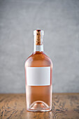 A single bottle of rose wine with an empty label stands on a wooden surface whose cork and neck hint at the refined contents, ideal for mock-ups.
