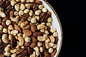 A delicious selection of mixed nuts, including almonds, pecans, hazelnuts and cashews, in a decorative bowl on a dark background - ideal for a healthy snack or as culinary inspiration