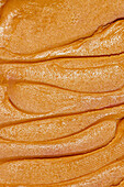 Eine Nahaufnahme, die die glatte, cremige Textur von frisch gestrichener Erdnussbutter mit ausgeprägten, gleichmäßigen Linien auf der Oberfläche zeigt.
