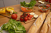 A selection of fresh ingredients such as tomatoes, lettuce, eggs, peppers and baguette on a wooden table, perfect for preparing a healthy meal.
