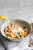 A ceramic bowl of cavatappi pasta topped with cheese, fresh spinach and a savoury tomato sauce. Next to the bowl is a glass of water with lemon and cutlery.