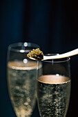 A close-up of Beluga caviar elegantly balanced on a spoon and placed over two bubbling champagne glasses against a dark background