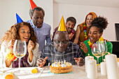 A cheerful group at a festive birthday party. The guest of honour wears a party hat and is ready to blow out the candles on the cake, surrounded by friends who rejoice with him.