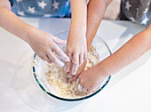 Two siblings are mixing dough in a transparent bowl and are engaged in a fun baking activity. Their hands are covered in flour, showing teamwork and creativity in the kitchen.