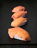 A selection of sushi pieces with salmon, elegantly presented on a black stone surface. Perfect for displaying authentic Japanese cuisine and culinary presentations.
