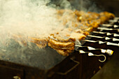 Fresh meat sizzling on a spit fills the air with smoke at a lively street festival and shows the lively atmosphere of food preparation.