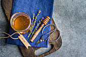 A jar of golden honey, sprigs of lavender and a wooden ladle rest on a blue cloth, creating a cheerful culinary scene The rustic chopping board and scissors add to the charm