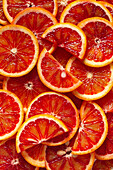A close-up of freshly sliced blood oranges, showing bright red and orange colours. The juicy segments form a pattern that emphasises the natural beauty and texture.