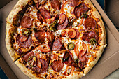 Draufsicht auf eine frisch gebackene Peperoni-Pizza mit Jalapenos, Tomaten und geschmolzenem Käse, die in einem Lieferkarton serviert wird und eine verlockende und köstliche Mahlzeit darstellt.
