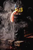 A visually captivating tiki cocktail, garnished with citrus fruits and colourful elements. Surrounded by ornate smoke, it is presented on rustic wood and creates a tropical ambience