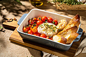 Delicious baked Camembert cheese, paired with roasted cherry tomatoes and crispy bread, garnished with herbs in a ceramic bowl, creates a rustic gourmet experience.