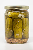 Close-up of pickled gherkins in a sealed jar with mustard seeds and pieces of onion against a white background. Ideal for food and preservation themes.