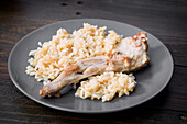 A delicious portion of baked rabbit paired with creamy rice on a dark grey plate The combination results in a rustic and hearty dish, perfect for a gourmet meal