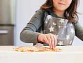 A young child in a star patterned apron carefully topping a homemade pizza with cheese in a warm kitchen environment that captures the joy of cooking and creativity.