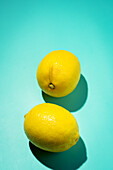 Two bright yellow lemons against a soft blue background that casts subtle shadows.