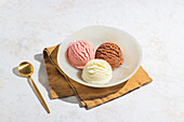 A close-up of three scoops of vanilla, chocolate and strawberry ice cream in a bowl, shot in soft natural light with a high-key aesthetic