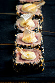 Close-up of rare tuna steaks sprinkled with sesame seeds, doused with mayonnaise and garnished with crispy onions The elegant presentation on a black slate emphasises the gourmet and artistic dish
