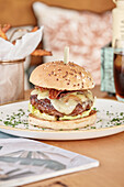 A close-up of a gourmet burger with melted cheese, crispy bacon and fresh salad on a sesame seed bun, served with fries and a refreshing drink
