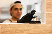 A baker with gloves can be seen in an Italian bakery, with the focus on a service bell on the counter. The warm ambience adds charm to the setting