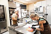 Two experienced pastry chefs work diligently in an Italian bakery, one mixing the ingredients and the other decorating a cake The bakery is lively and well-equipped