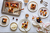 Top view of a sweet dessert table with pieces of cake decorated with cherries, blackberries and whipped cream, accompanied by cups of coffee. A rustic ambience completes the homely atmosphere, ideal for a cosy afternoon snack.