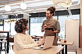 A friendly café scene in which a barista helps a customer with their order using a tablet.