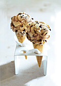 Two ice cream cones filled with banana split ice cream in a white ice cream stand on a beige background