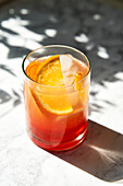 Aperol Spritz on marble surface with shade and hard sunlight, garnished with orange slice