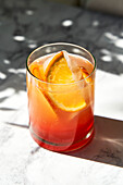 Aperol Spritz on marble surface with shade and hard sunlight, garnished with orange slice