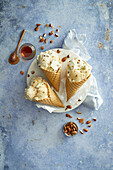 Almond and honey ice cream, prepared in three crunchy ice cream cones, arranged on a white plate, decorated with almonds and honey on a blue background