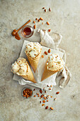Almond and honey ice cream, prepared in three crunchy ice cream cones, served on a white plate, decorated with almonds and honey on a beige stone background