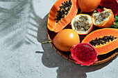 Exotische tropische Früchte, Passionsfrüchte und Drachenfrüchte, reife Papayas. auf einem Bambustablett mit grünen Blättern, Hintergrund aus Stein