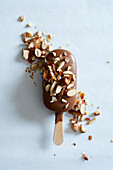 Almond ice cream on a stick covered in milk chocolate and sprinkled with roasted almonds on a white marble background