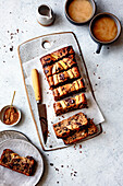 View from above of a sliced banana bread with chocolate chips on a wooden cutting board, accompanied by coffee and a small bowl of brown sugar.