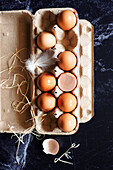Fresh eggs in a carton on a black marble background.