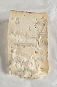 A piece of Italian cheese called 'Gorgonzola' lying on the paper in which it is wrapped. Front view.