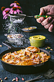 Side view of a cast-iron pan with curled phyllo, action with male hand holding a sieve with icing sugar