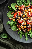 Salat mit Kichererbsen, schwarzem Reis, Tomaten, Mandeln und Grünzeug auf einem schwarzen Teller. Schwarzer Hintergrund