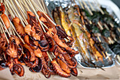 Close-up of grilled octopus skewers at a street market. Seafood delicacy with tentacles on wooden sticks. Freshly cooked fish can be seen in the background. Asian cuisine.